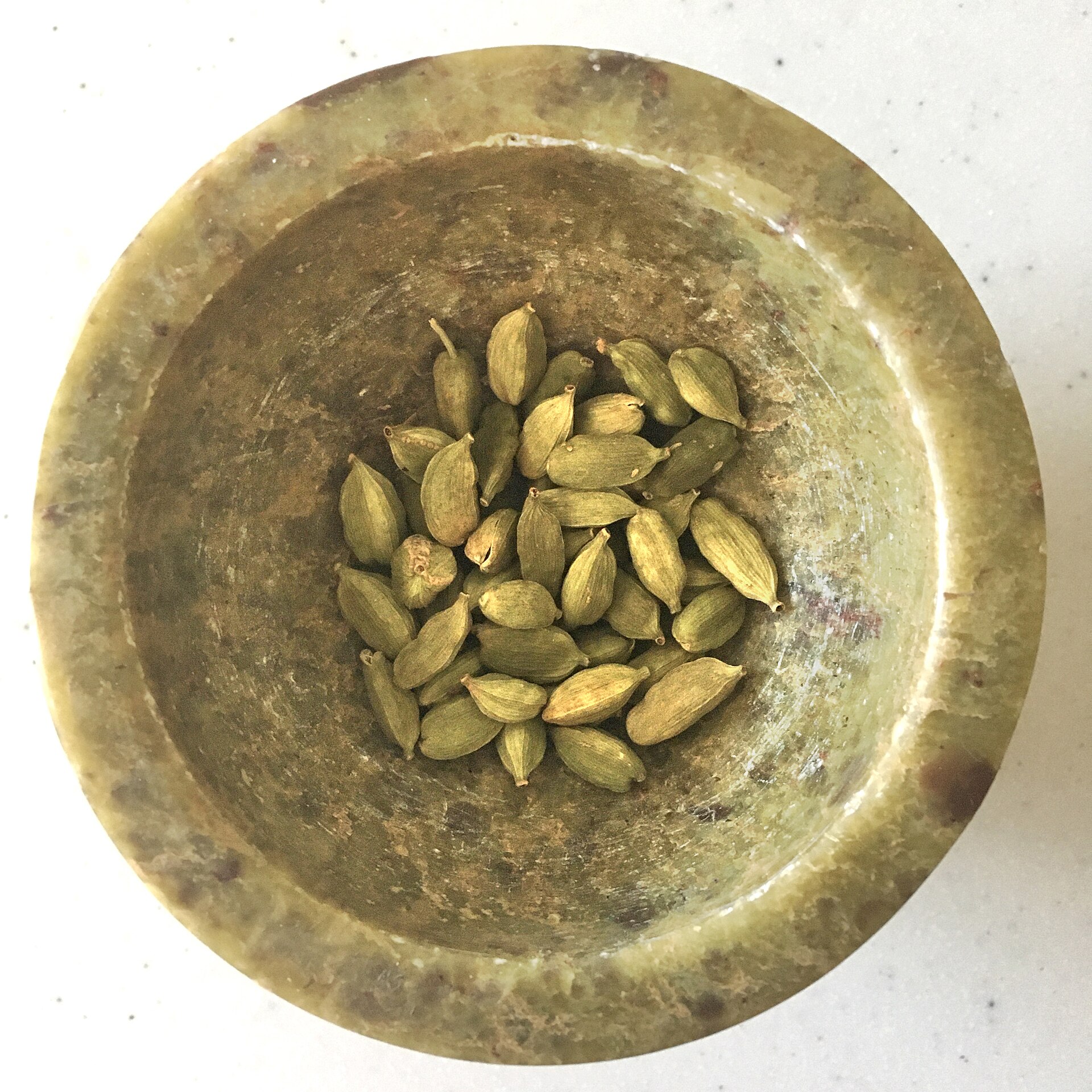 Green cardamom pods in a stone bowl